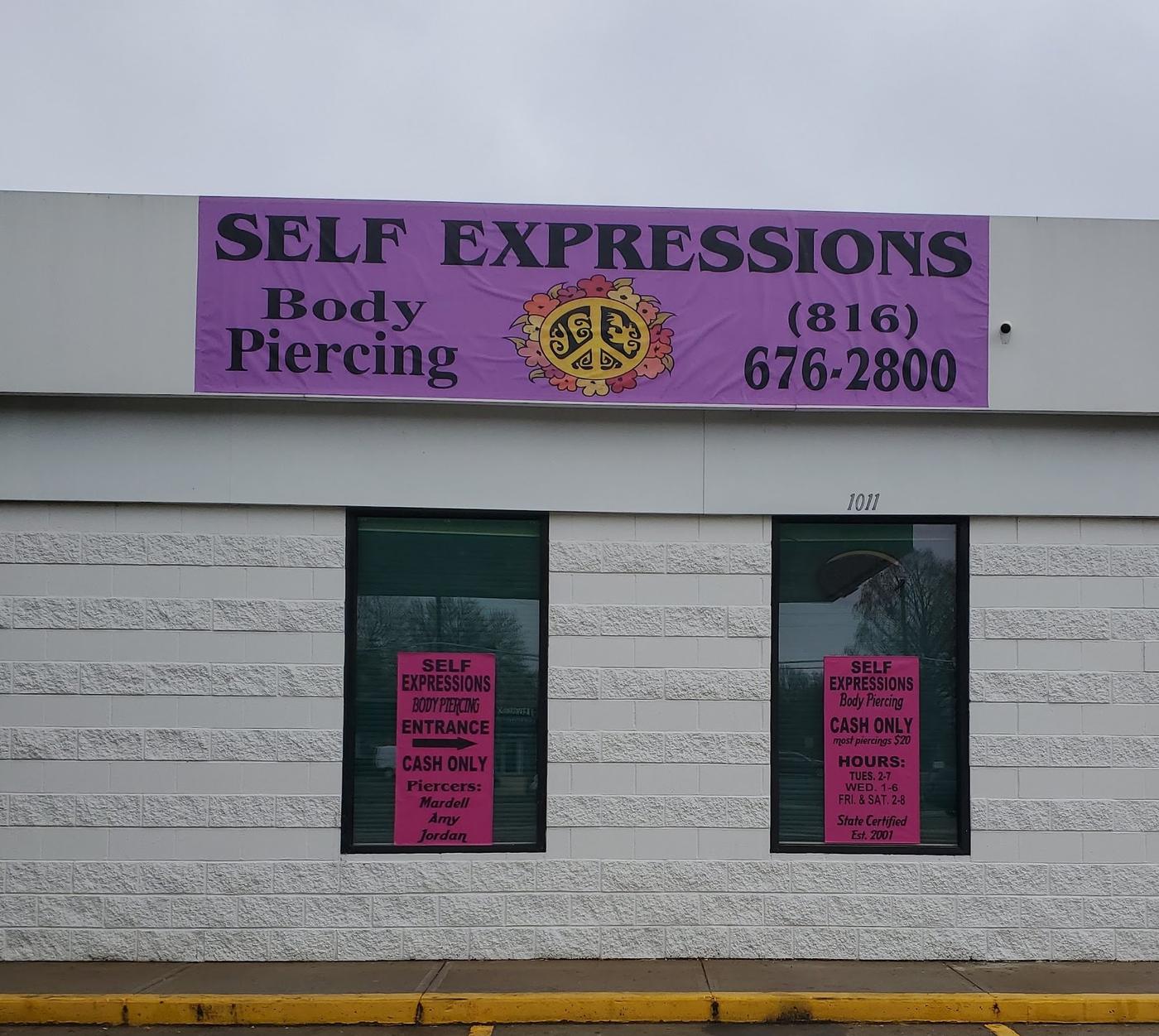 The front of Self Expressions: a white block building with a purple banner reading Self Expressions Body Piercing and the phone number, and two pink signs in the windows.