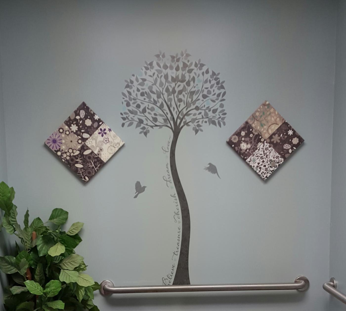A pale green wall with a painted tree decal and two quilted fabric panels, beside a grab rail.